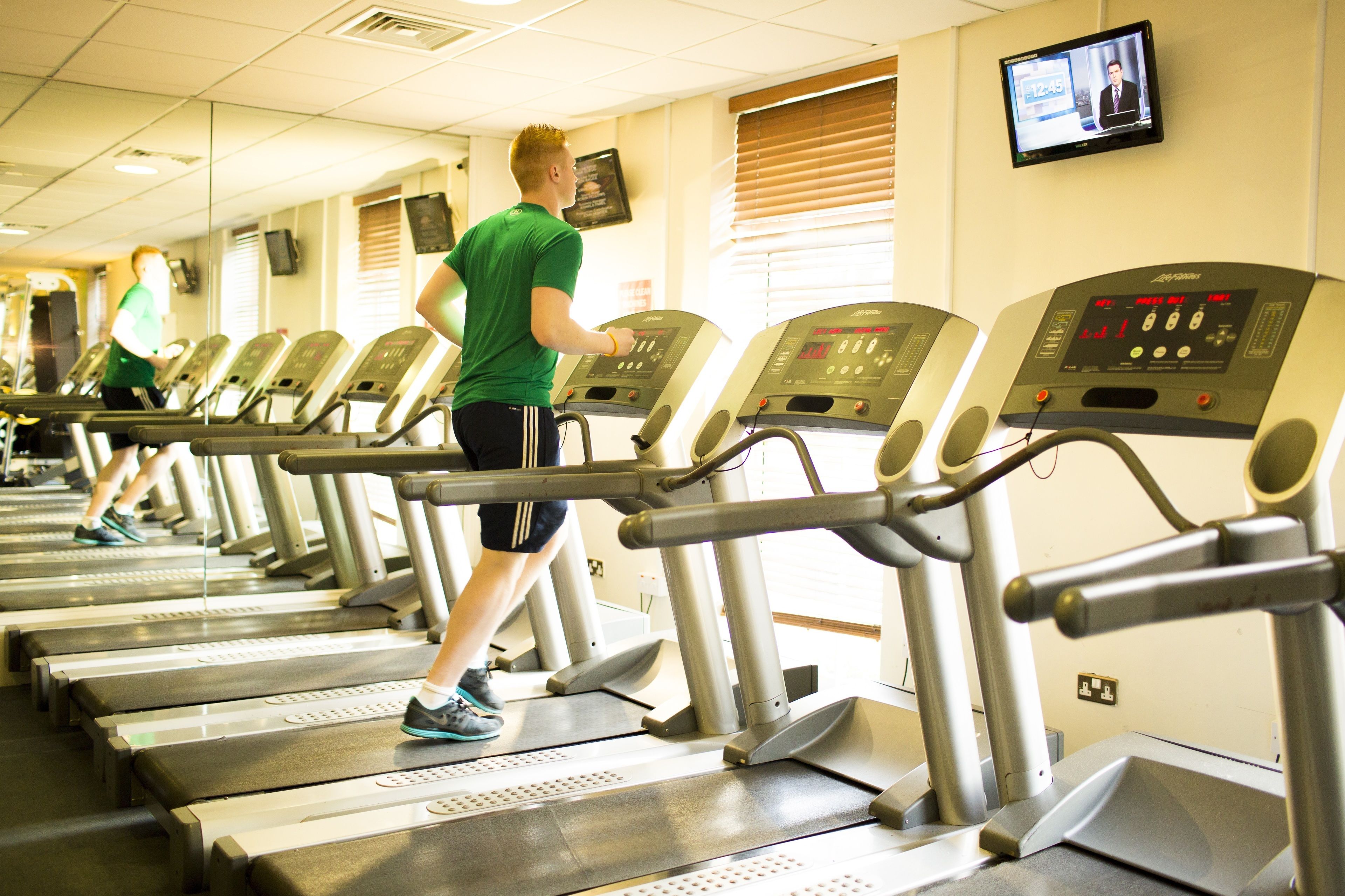 A row of treadmills in a gym with a television mounted on the wall.