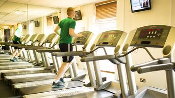 A row of treadmills in a gym with a television mounted on the wall.