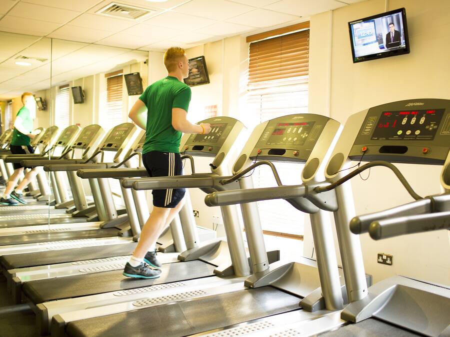 A row of treadmills in a gym with a television mounted on the wall.