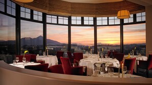 Un restaurante con una mesa dispuesta para comer, ventanas amplias y vistas al atardecer.