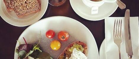 A breakfast setting with toast, tomatoes, spinach, and a poached egg on a plate, a cup of tea, and a glass of orange juice on a table.