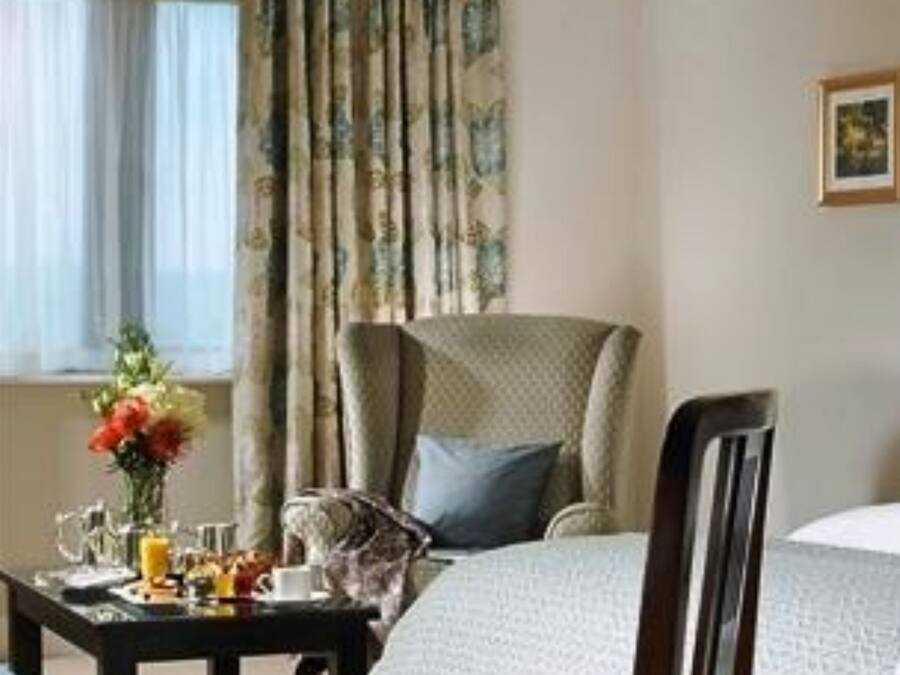 A hotel room with a bed, a chair, a table with breakfast items, and a window with curtains.