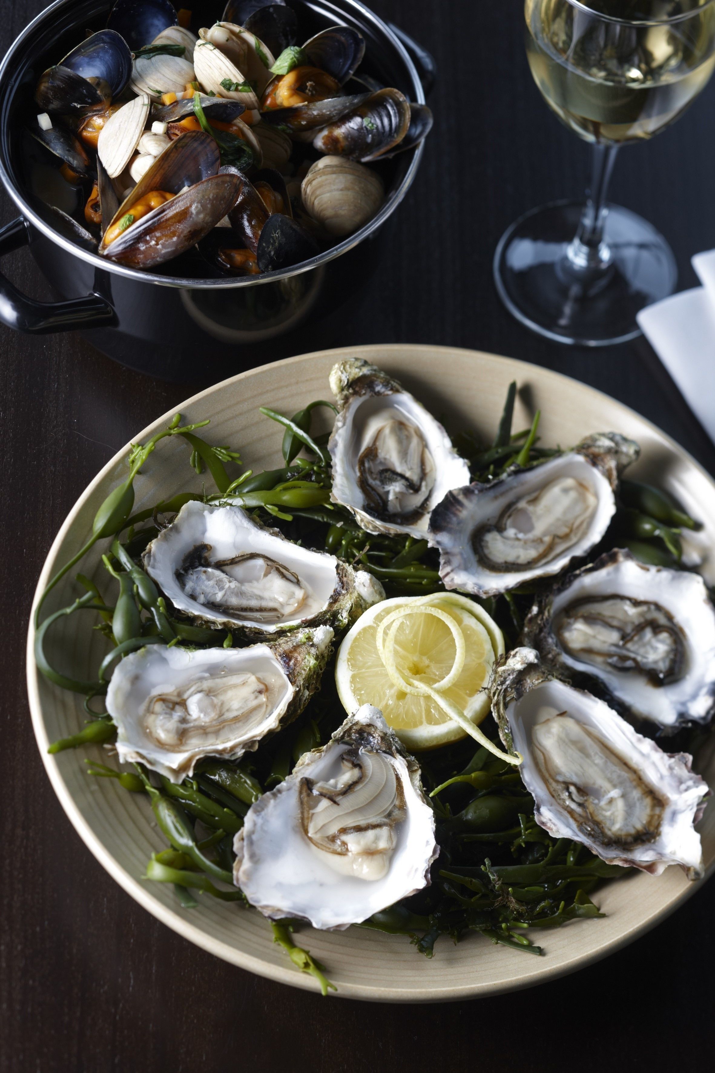 Een bord met oesters, citroen en groene garnering, en een kom met mosselen op de achtergrond.