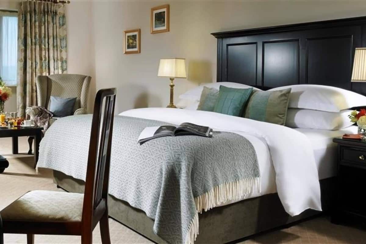 Una habitación de hotel con una cama, una silla, un escritorio con una lámpara y una mesita de noche con lámpara.