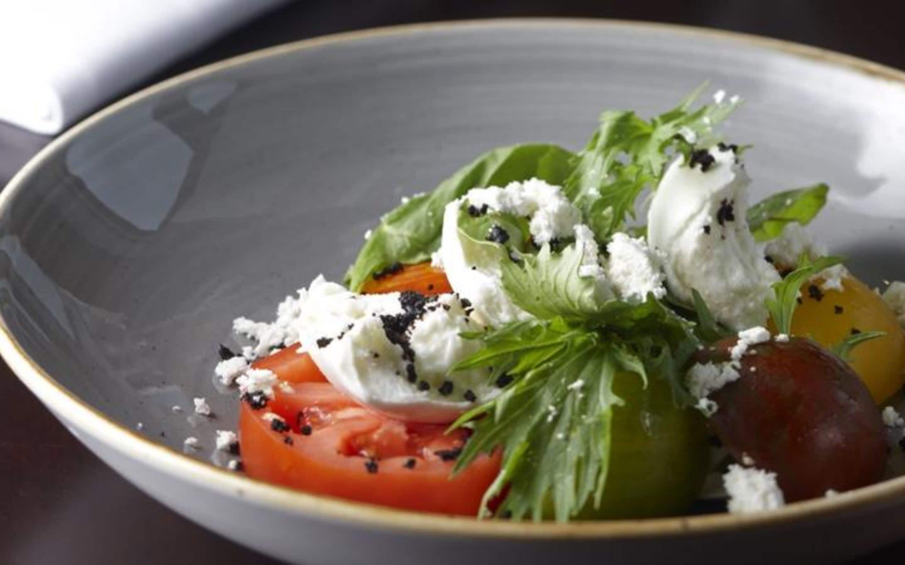 A bowl of salad with tomatoes, greens, and cheese.