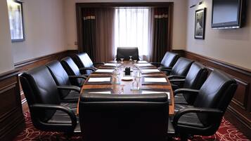 A conference room with a long table, black leather chairs, a wooden table, and a TV on the wall.
