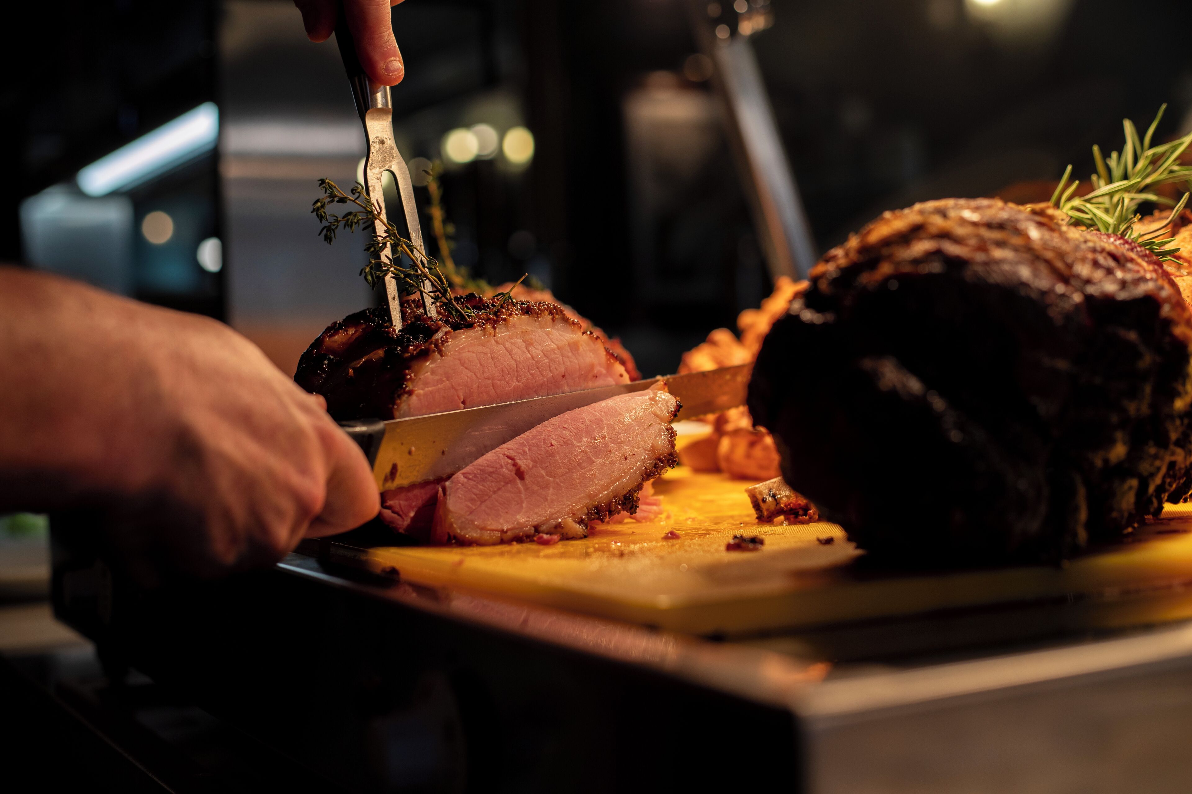 Una persona cortando un plato de carne cocida, probablemente un asado, sobre una tabla de cortar.