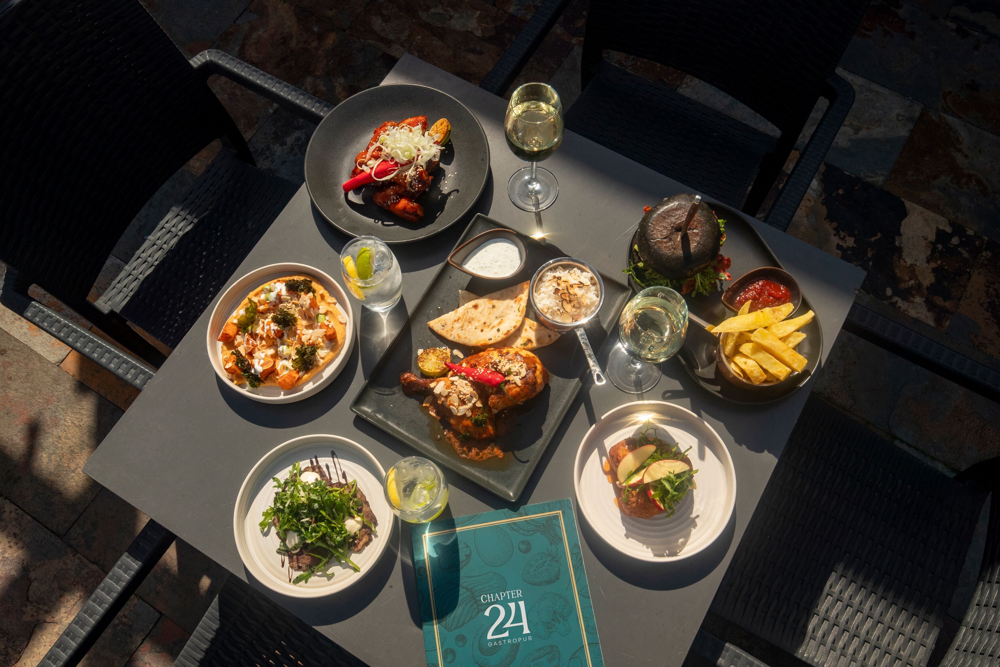 A table set with various dishes, a wine glass, and a menu titled 'Chapter 24 GastroPub.'