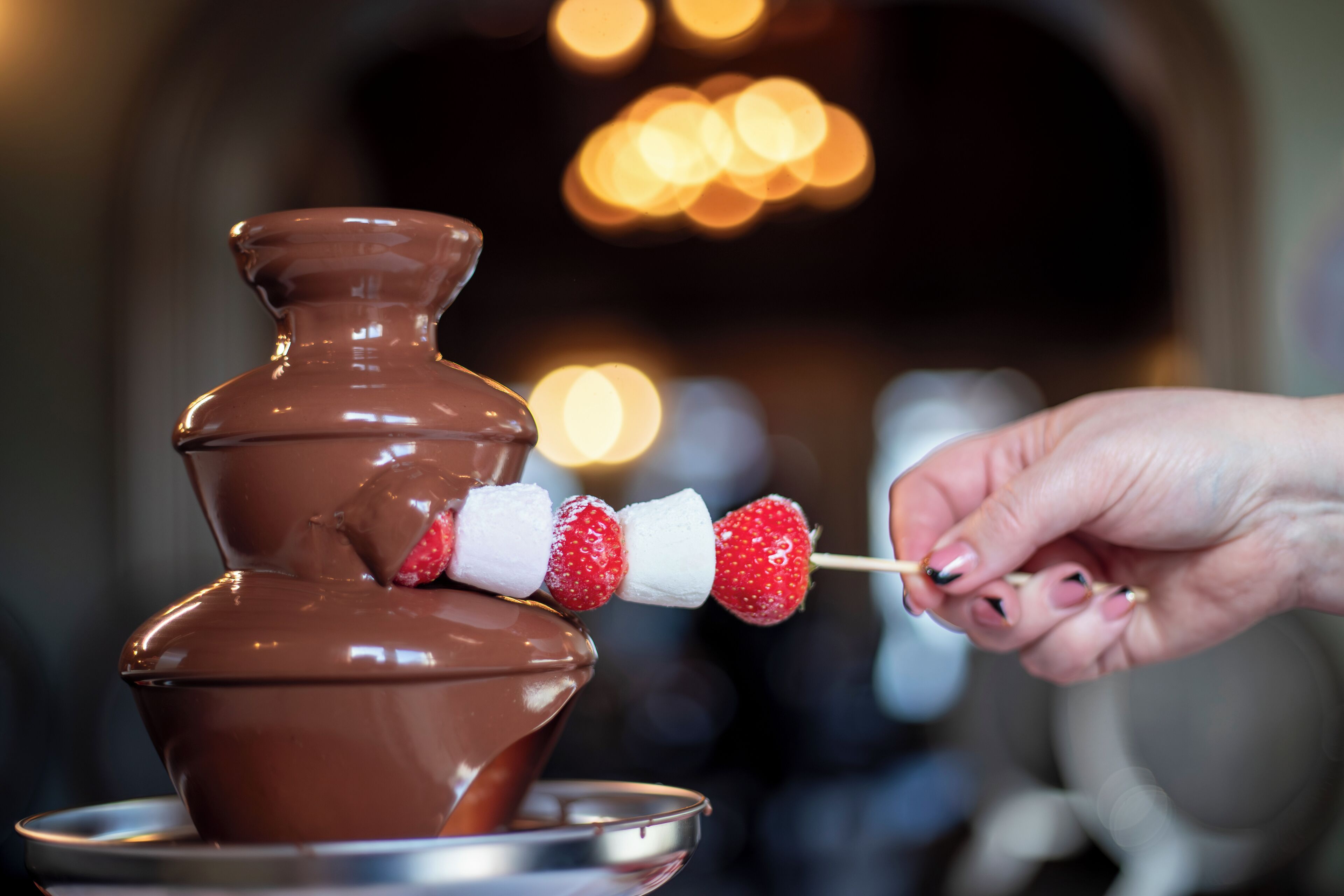 A chocolate fountain with strawberries and marshmallows being dipped.