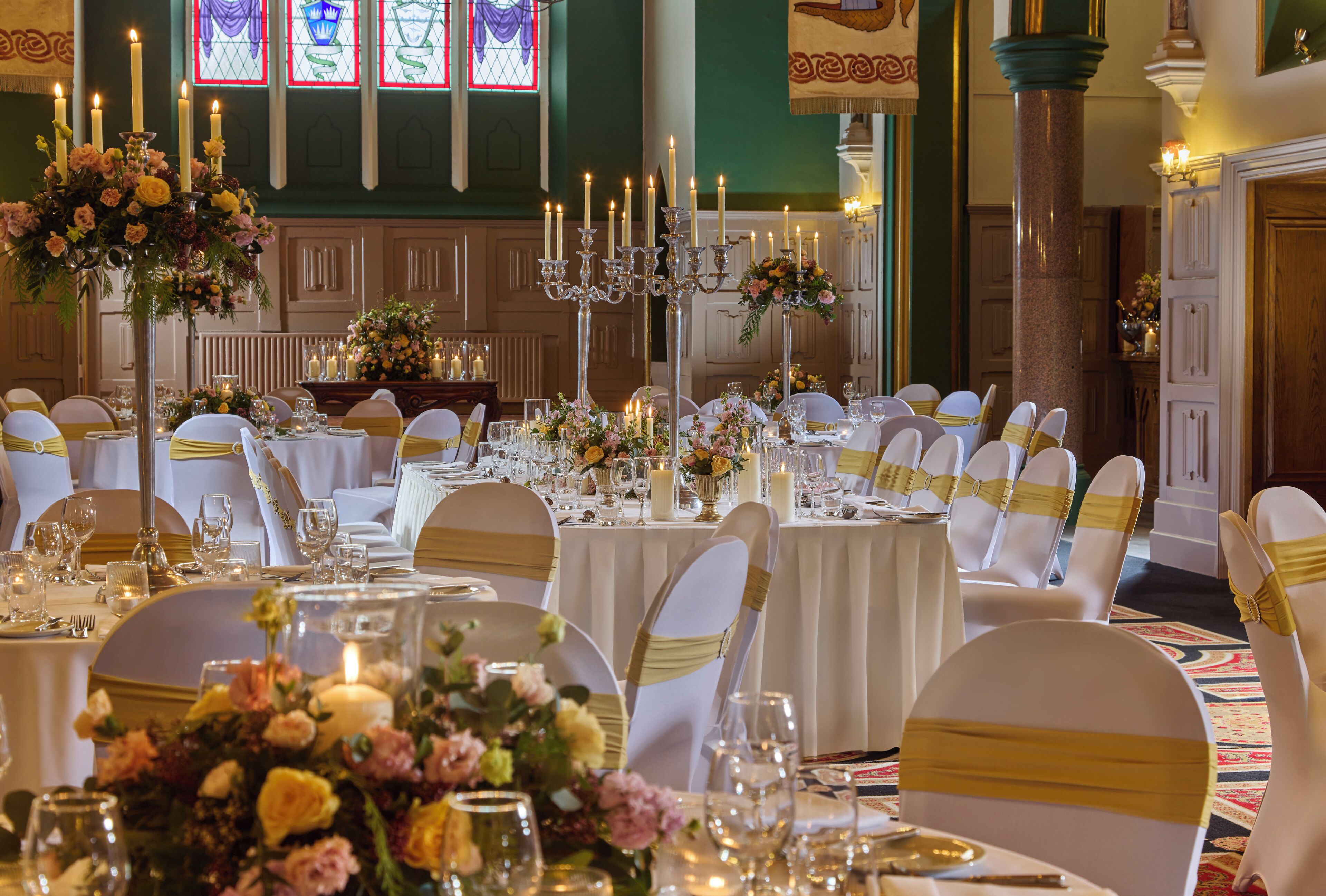 A banquet hall with round tables, white chairs, and floral centerpieces.