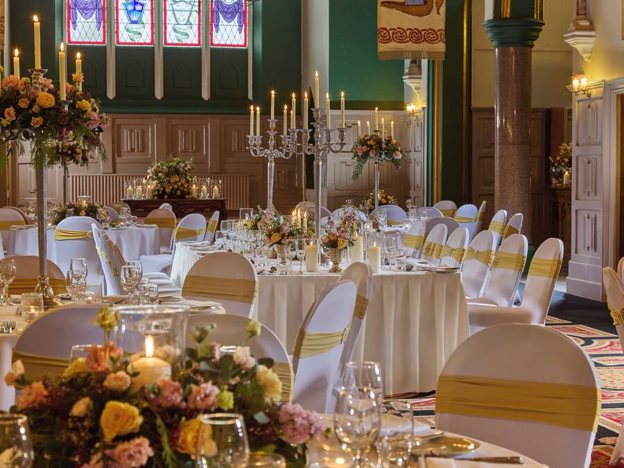 A banquet hall with round tables, white chairs, and floral centerpieces.