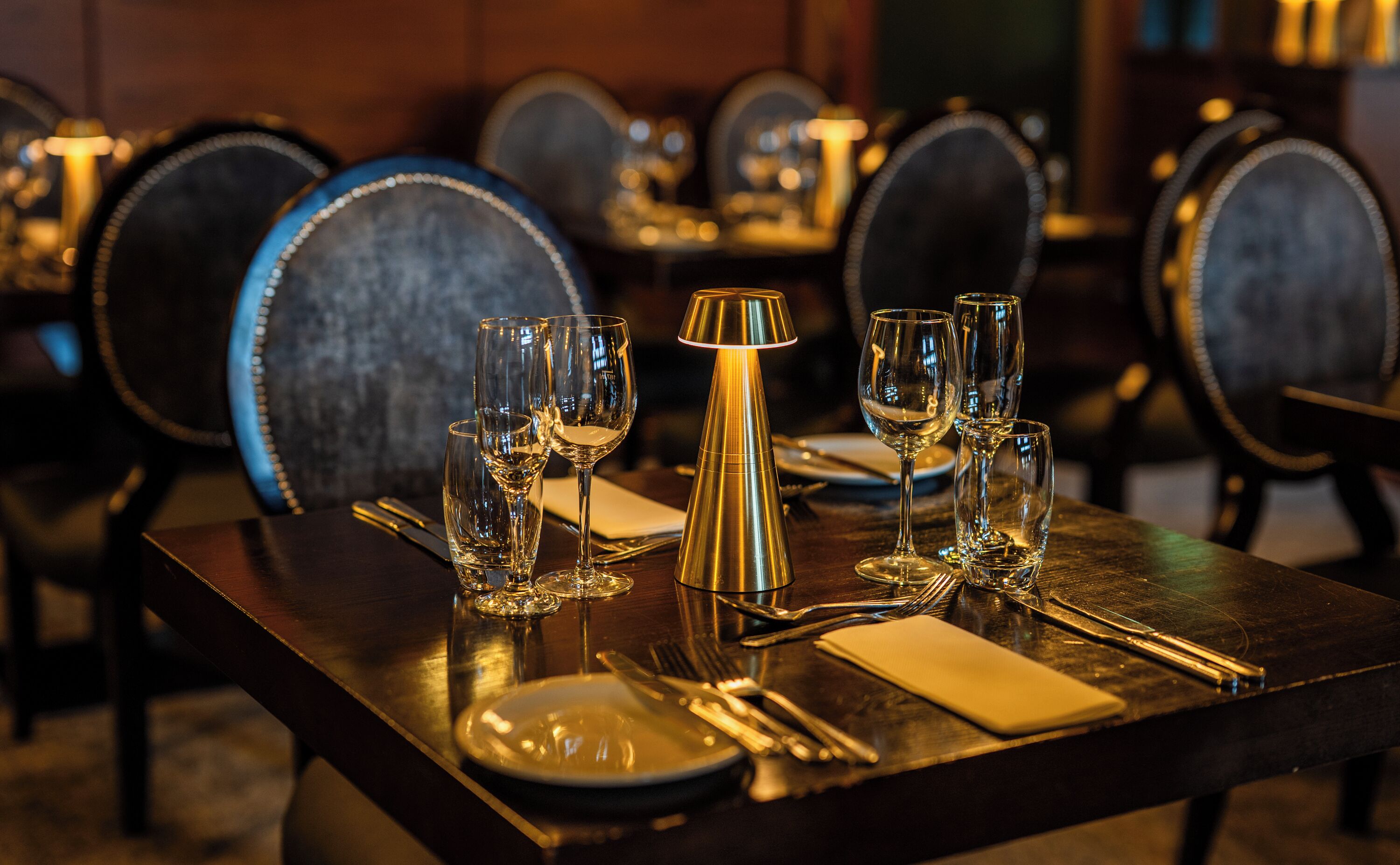 Una mesa de comedor dispuesta con copas de vino, un centro de mesa dorado y cubertería ordenada.