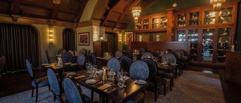 Un comedor formal con mesas de madera, sillas tapizadas y una bodega con puertas de vidrio.