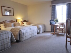 A hotel room with two beds, a small table with a chair, a framed picture on the wall, and a window with curtains.