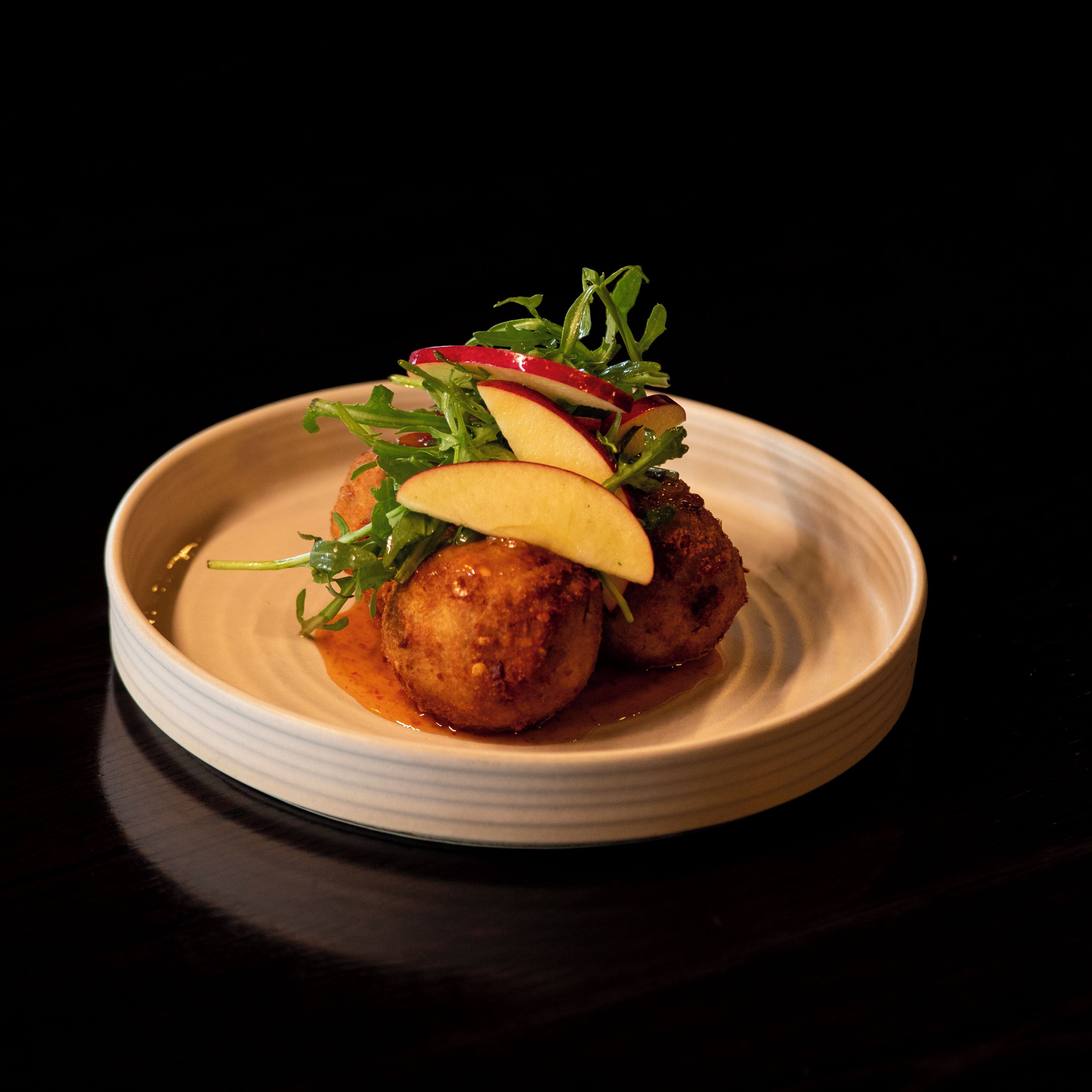 A plate with food, including meatballs and apple slices, on a white plate.