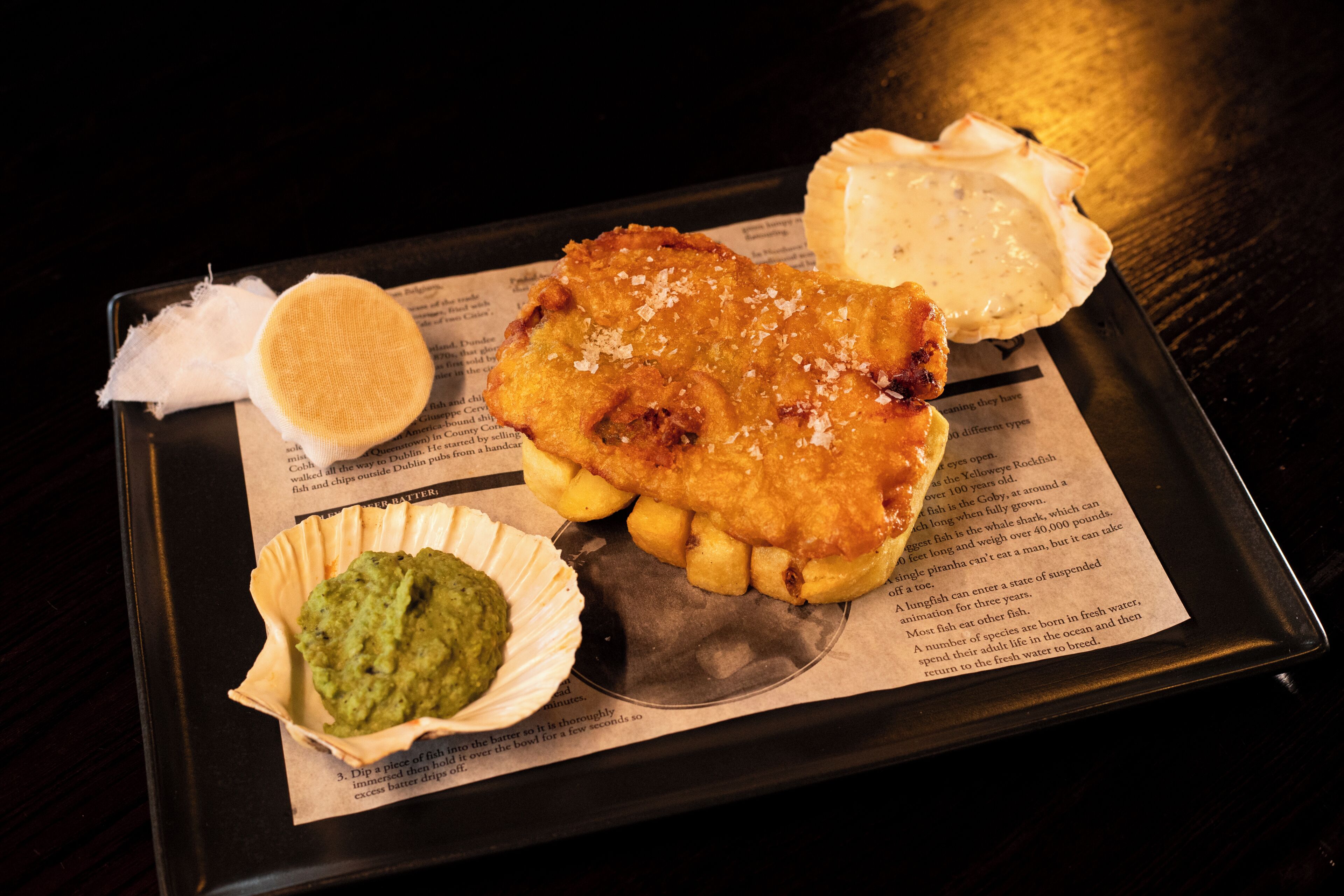 A tray with a fish fillet, chips, mushy peas, and tartar sauce.