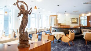 A dining area with tables and chairs, a statue on a wooden pedestal, and a bar area with a sofa.