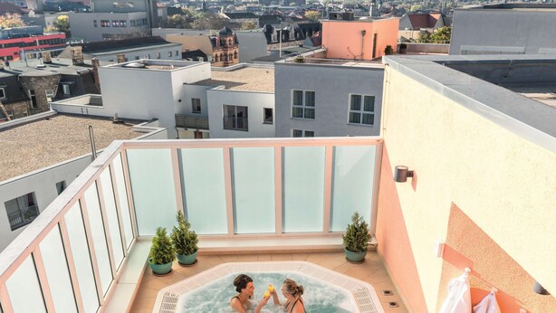 A rooftop terrace with a hot tub, potted plants, and a view of the cityscape.