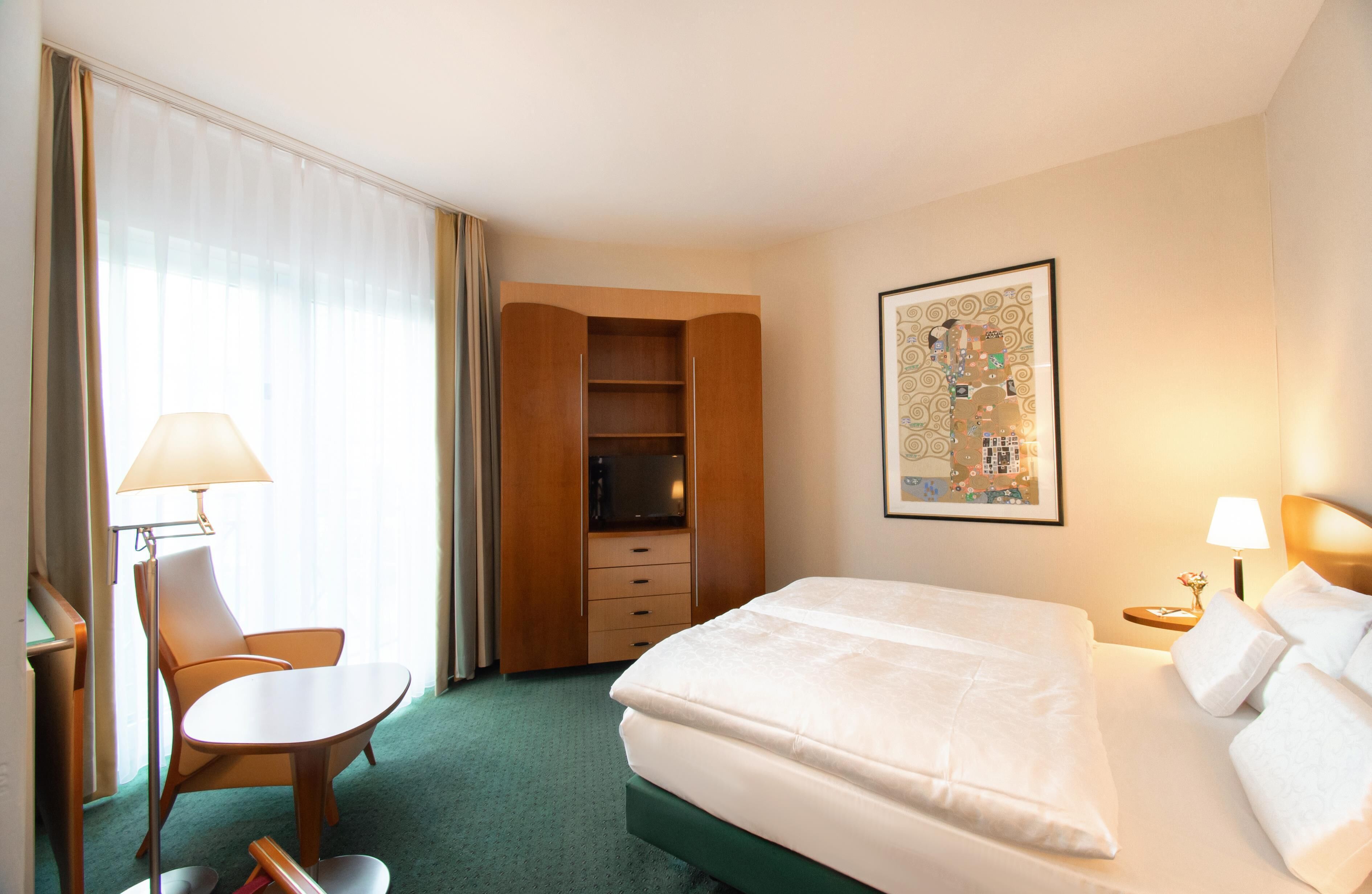Habitación de hotel con cama, escritorio, silla, armario y un cuadro en la pared.