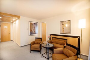 Habitación de hotel con cama, dos sillas, una mesita y obras de arte en las paredes.