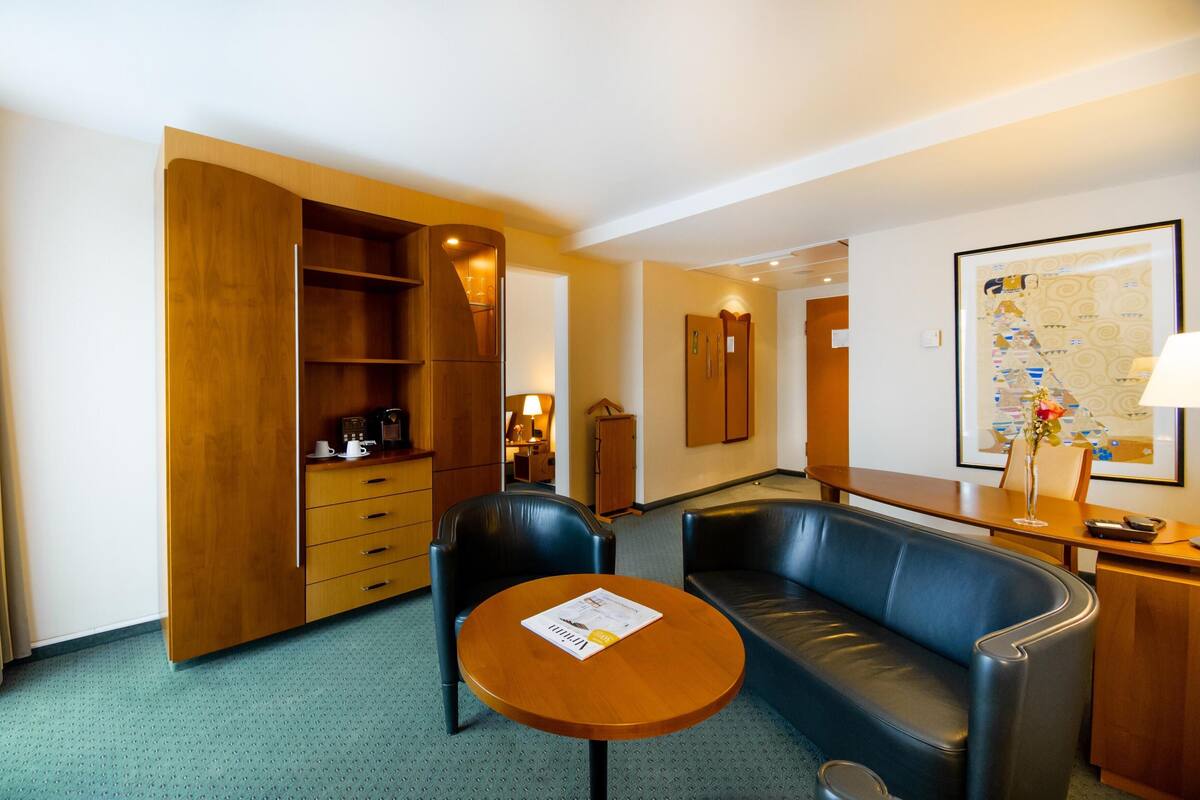 Een hotelkamer met een bank, een klein rond tafeltje, een houten kast en een spiegel aan de muur.