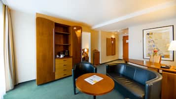 Habitación de hotel con sofá, un aparador de madera, una mesita con una revista y un cuadro en la pared.