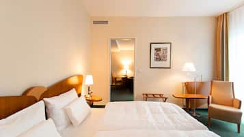 A hotel room with a large bed, a chair, a desk, and a small table.