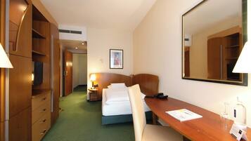 Habitación de hotel con cama, escritorio, silla, lámpara, teléfono, espejo y armario.