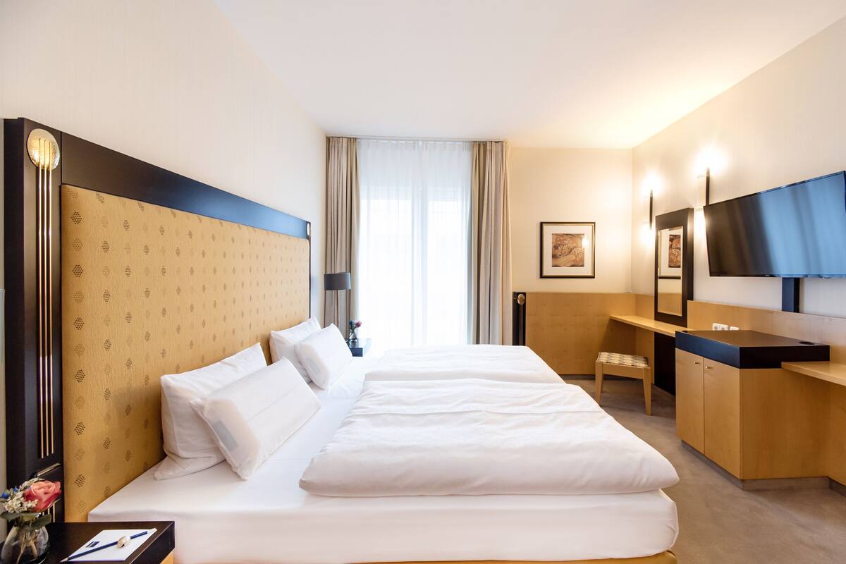Een hotelkamer met een groot bed, een bureau, een stoel, een televisie en een raam met gordijnen.