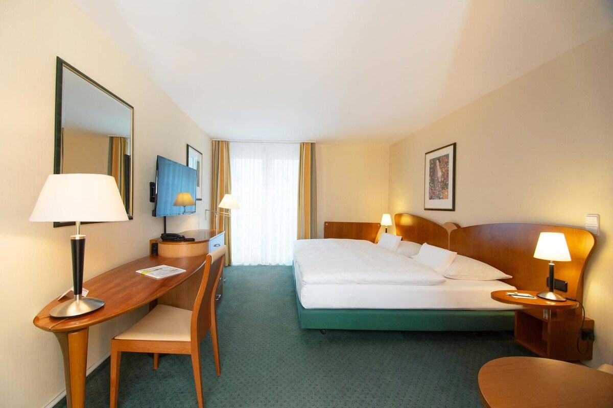 A hotel room with a bed, desk, chair, and a television.