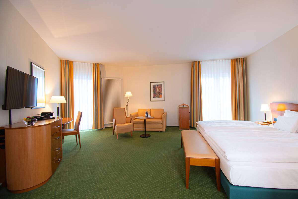 Een hotelkamer met een bed, een bureau, een stoel, een bank, een televisie en een raam met gordijnen.