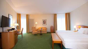 A hotel room with a bed, a desk, a chair, a sofa, a television, and a window with curtains.