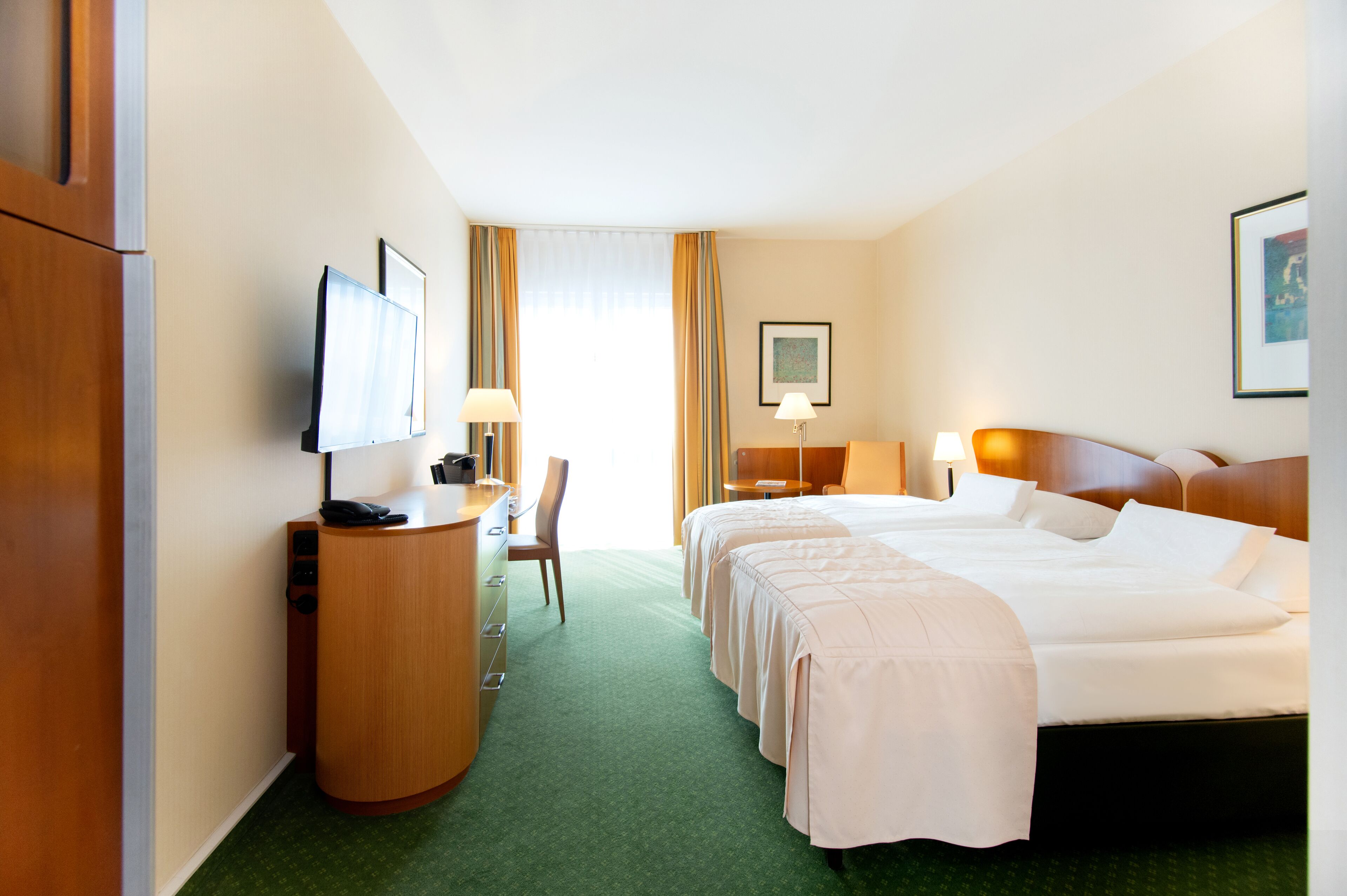 Een hotelkamer met twee bedden, een bureau met telefoon, een stoel en een televisie aan de muur.