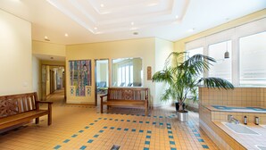 A spacious lobby with a tiled floor, a wooden bench, a large potted plant, and a reception area with a sink.