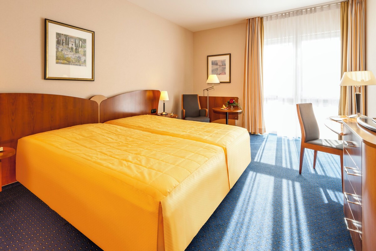 A hotel room with two beds, a desk, a television, and a window with curtains.