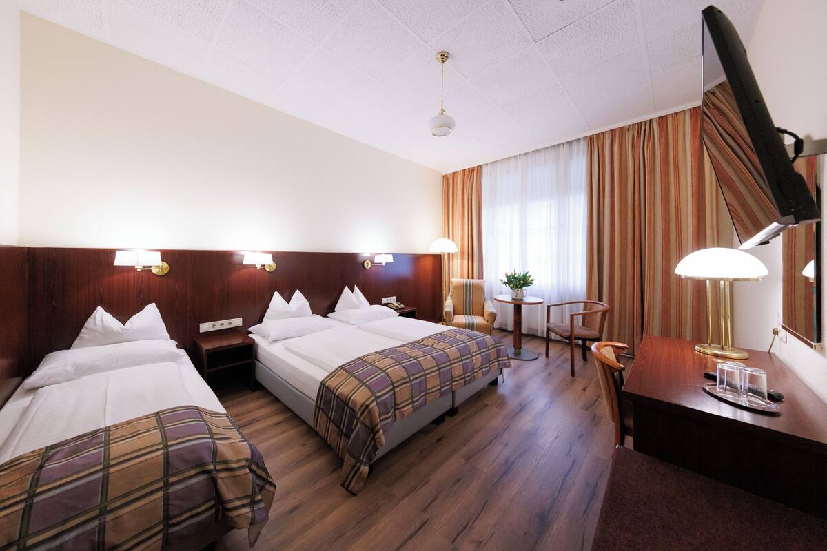A hotel room with two beds, a desk, a chair, a lamp, and a window with curtains.