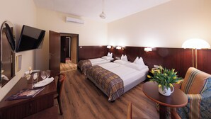 A hotel room with two beds, a desk with a chair, a TV, a table with a plant, and a lamp.
