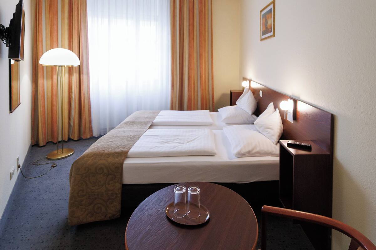A hotel room with two beds, a desk, a chair, a lamp, and a TV.