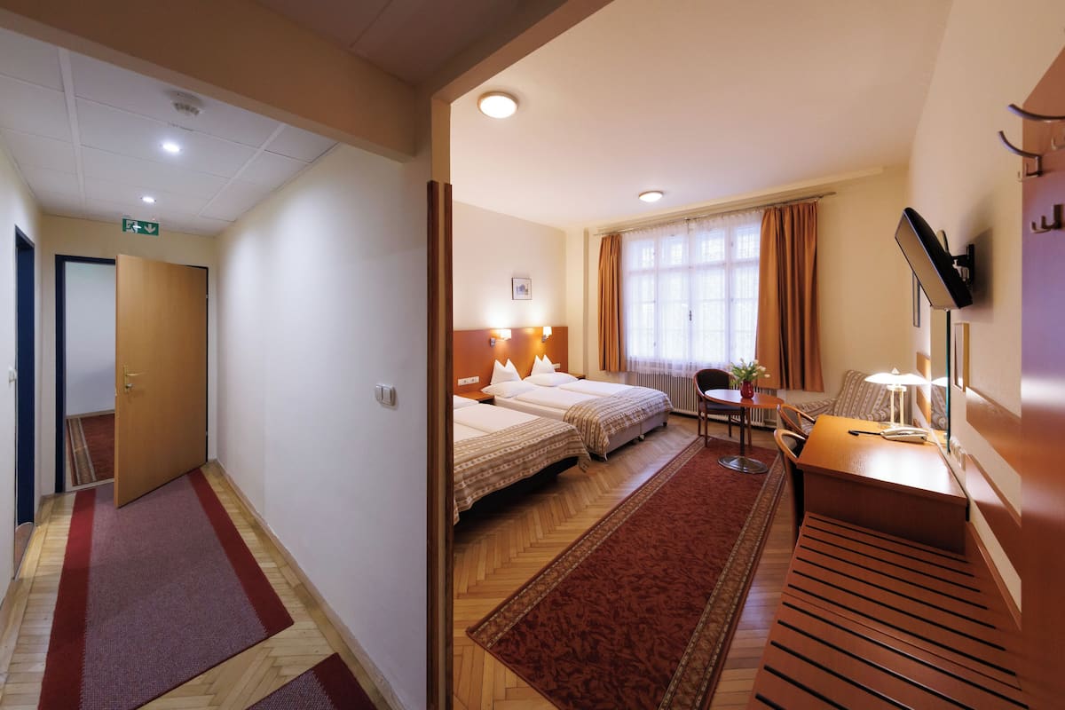 A hotel room with two beds, a desk, a chair, a TV, and a window with curtains.