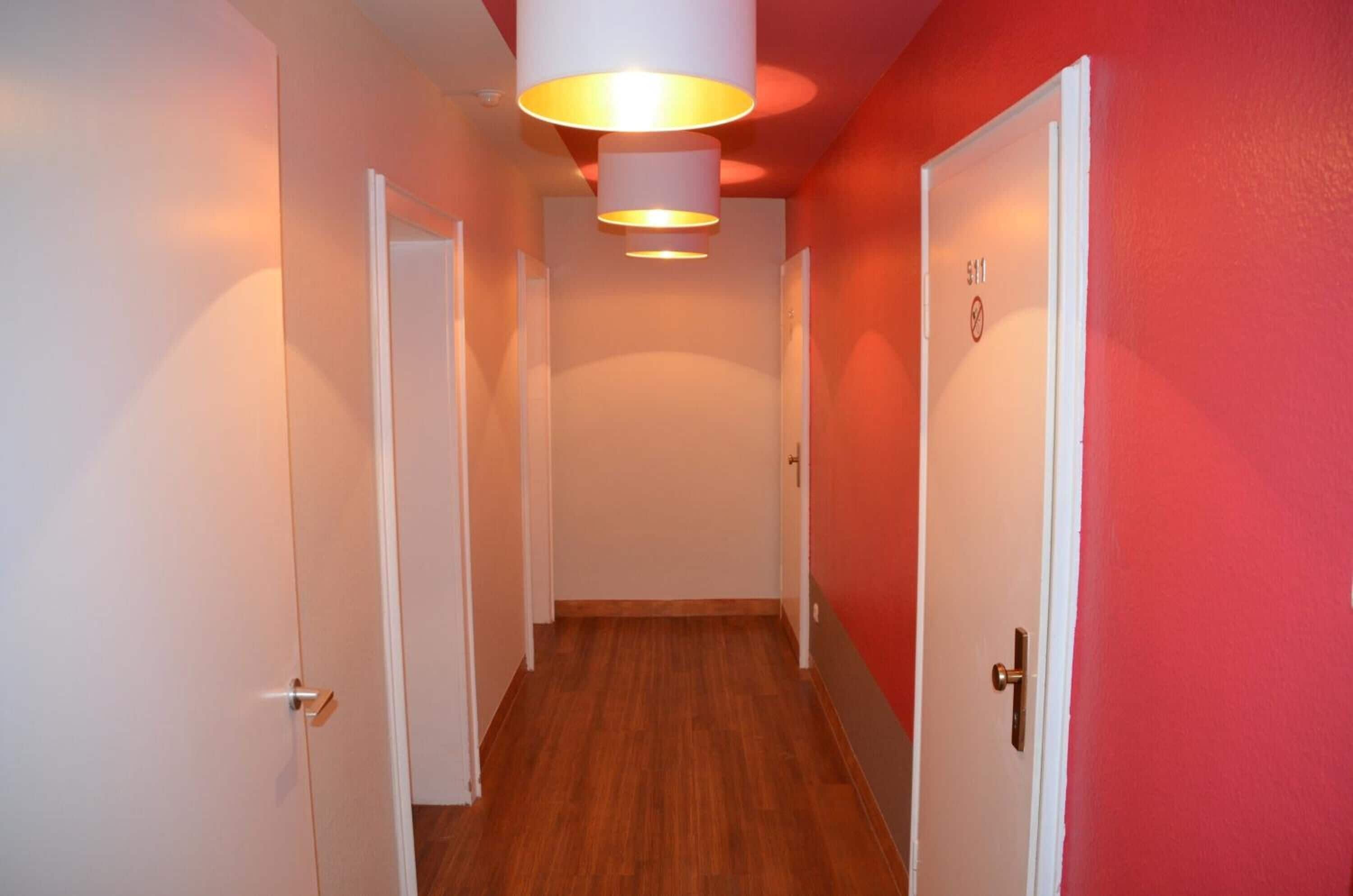 Un pasillo con suelo de madera, puertas blancas y una pared roja.