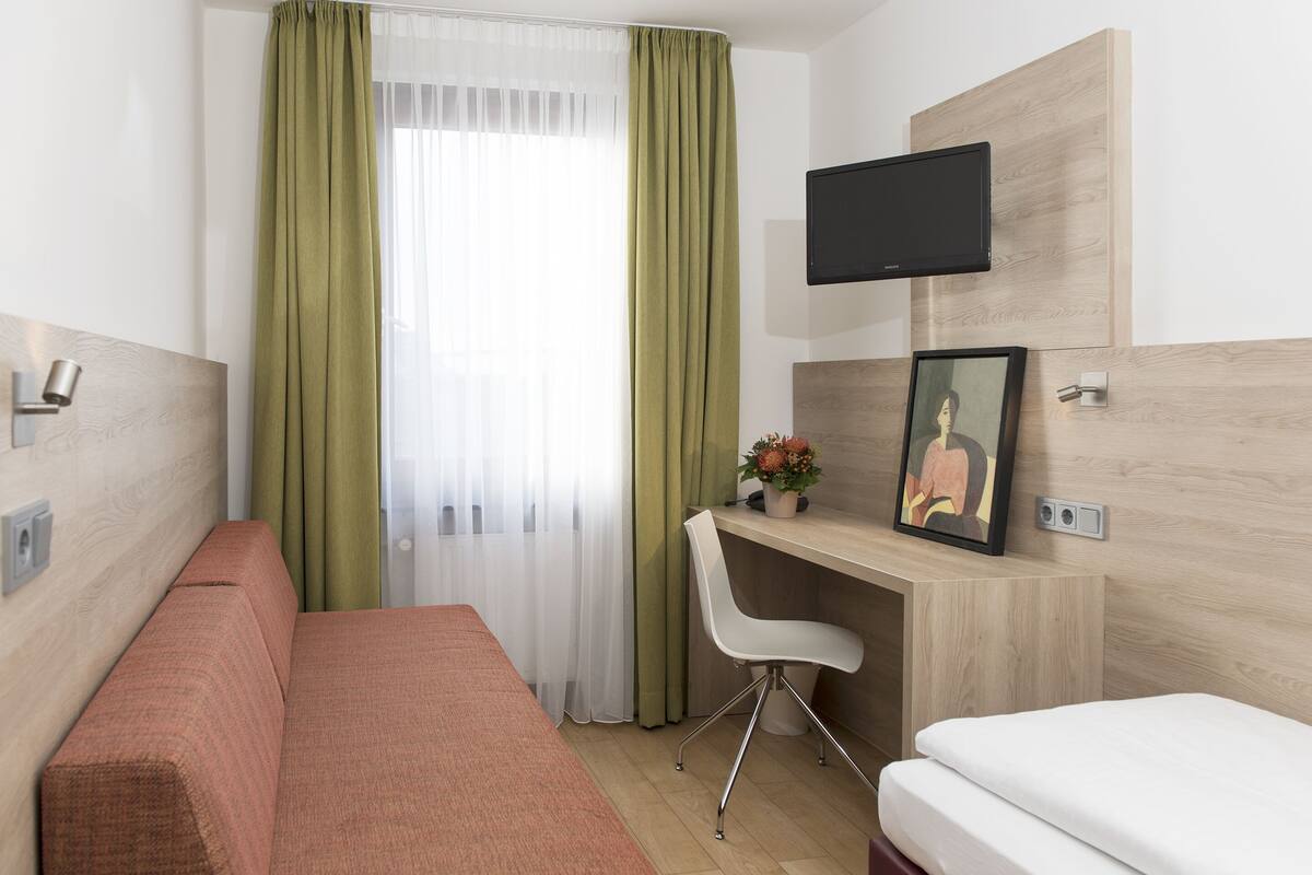 A hotel room with a bed, a desk with a chair, a TV, and a picture on the wall.