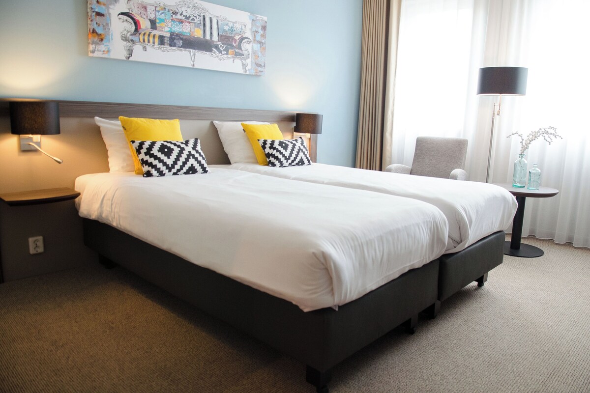 A hotel room with a large bed, two bedside tables, a chair, and a floor lamp.