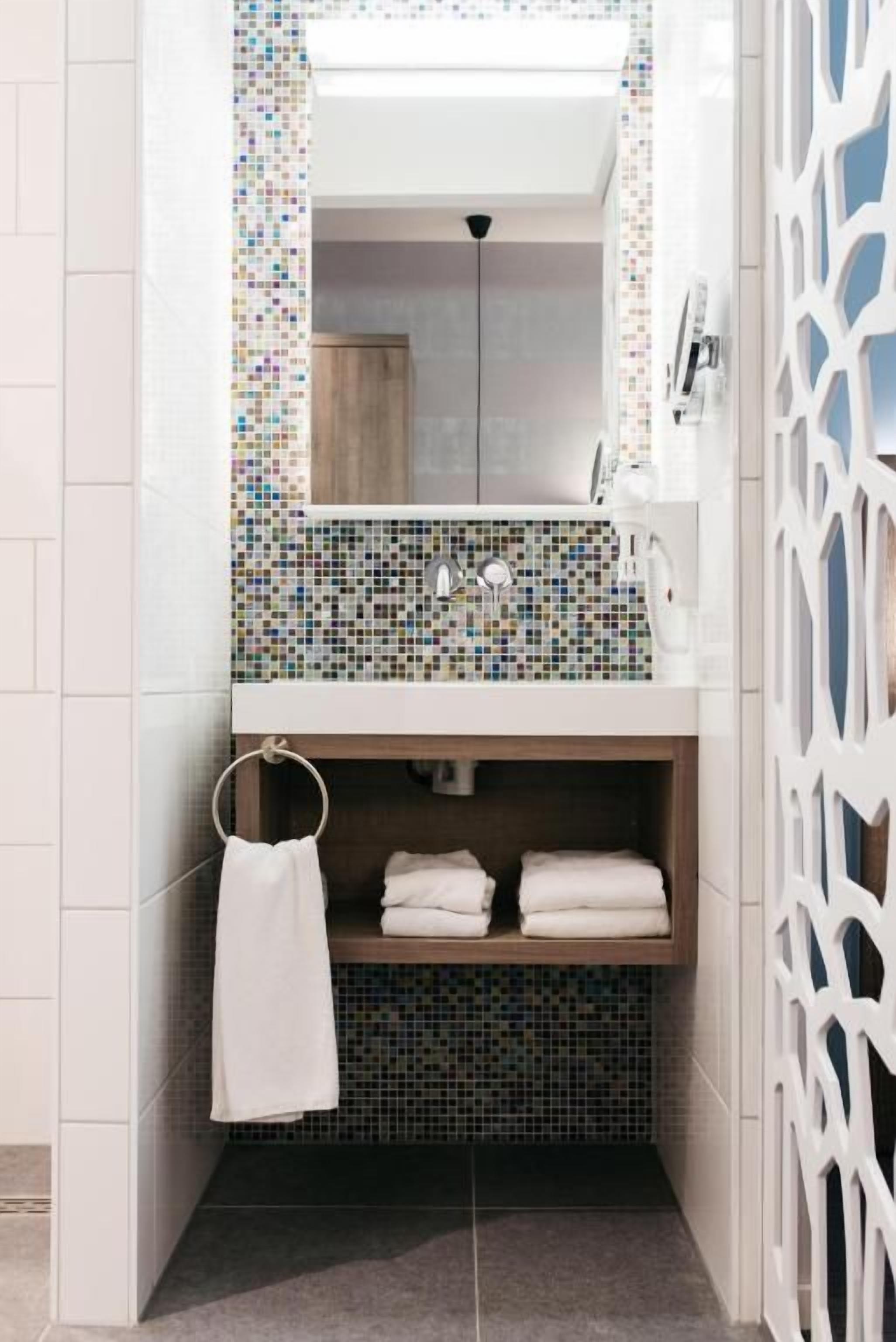 A bathroom with a tiled backsplash, a mirror, a towel rack, and a shelf with folded towels.