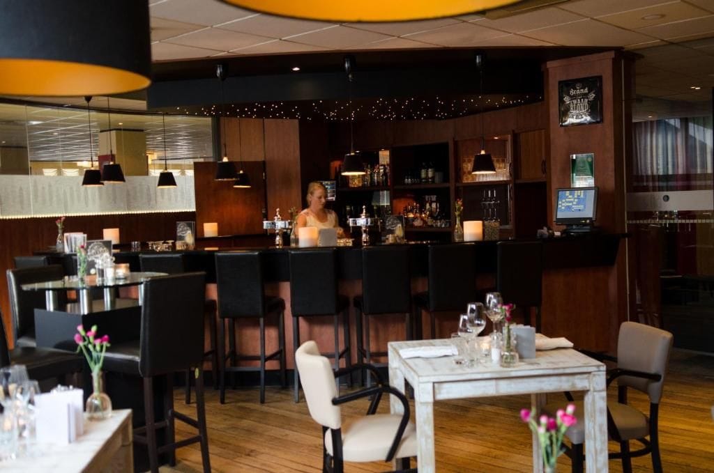 A bar area with a bartender, wooden bar counter, and seating with tables and chairs.