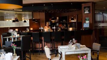 Un espace bar avec un barman, un comptoir en bois et des tables et des chaises pour s’asseoir.