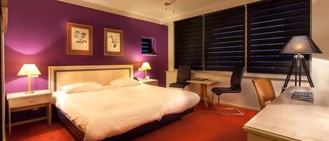 A hotel room with a bed, two bedside tables, a desk, a chair, a lamp, and a ceiling fan.