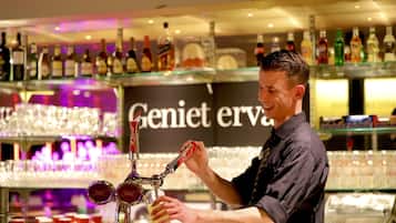 En bartender hælder en drink i baren, baggrunden viser et udvalg af flasker og glas.