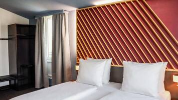 Een hotelkamer met een bed, een bureau, een stoel en een raam met gordijnen.