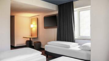 A hotel room with two beds, a TV, a mirror, and a window with curtains.
