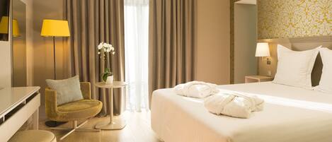 Habitación de hotel con cama, escritorio, silla, lámpara y una mesita con una planta.
